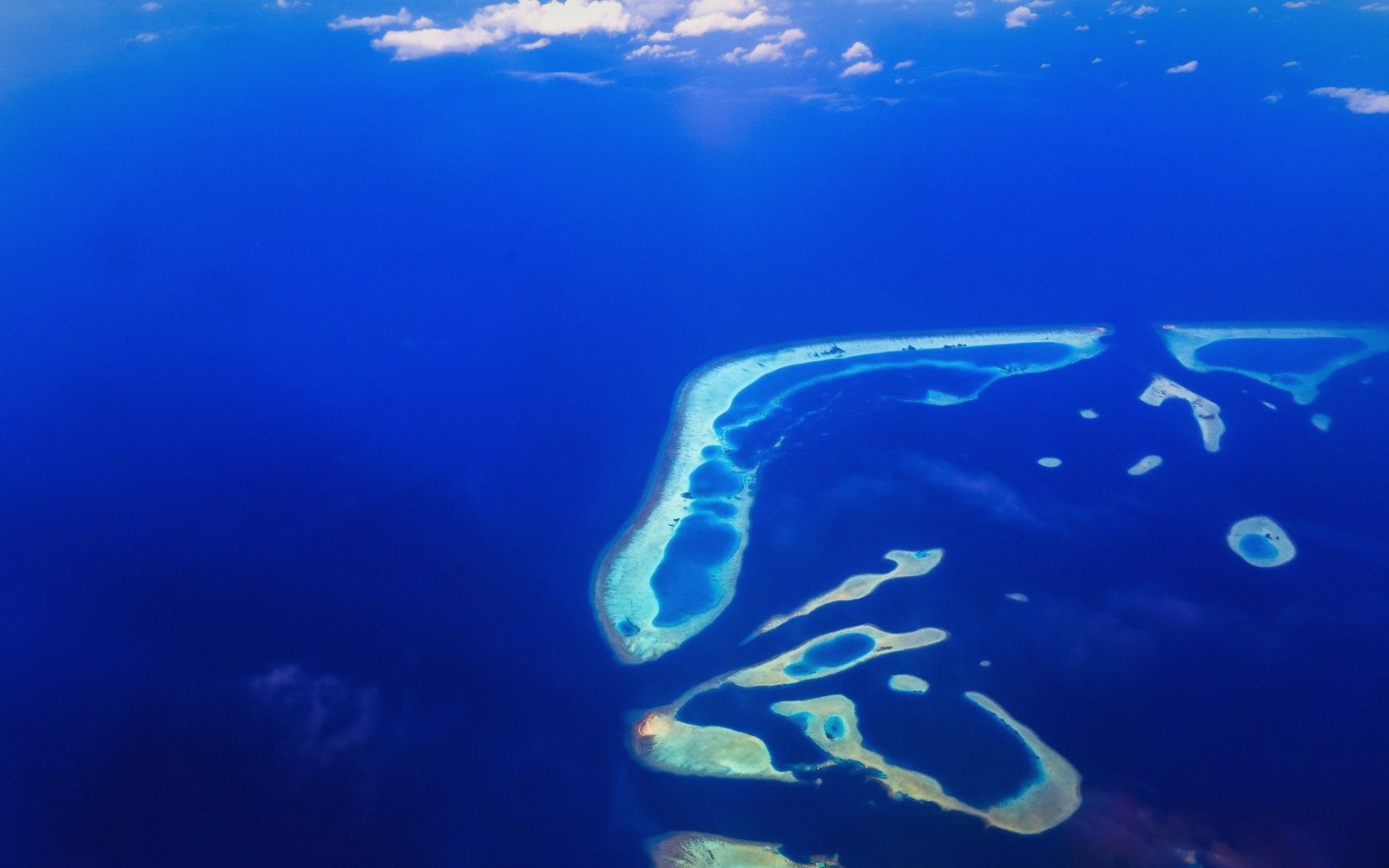 Aerial view of a curving coral atoll surrounded by deep blue ocean water