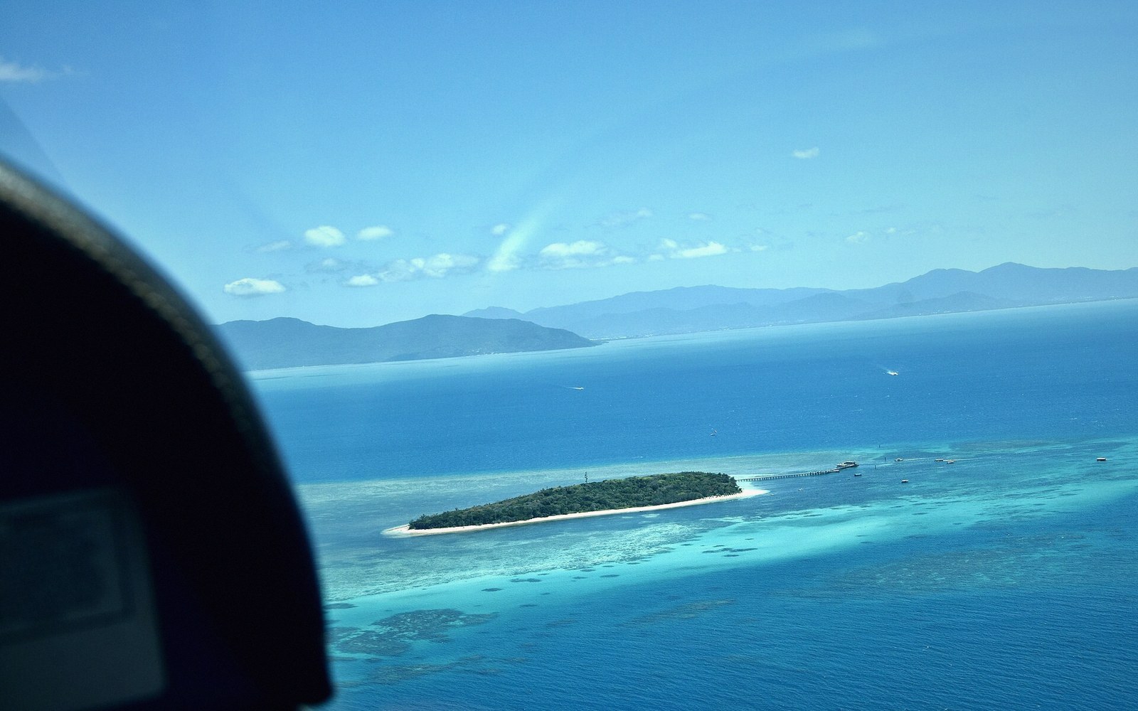 Aerial view from a plane window of a small reef island surrounded by turquoise water